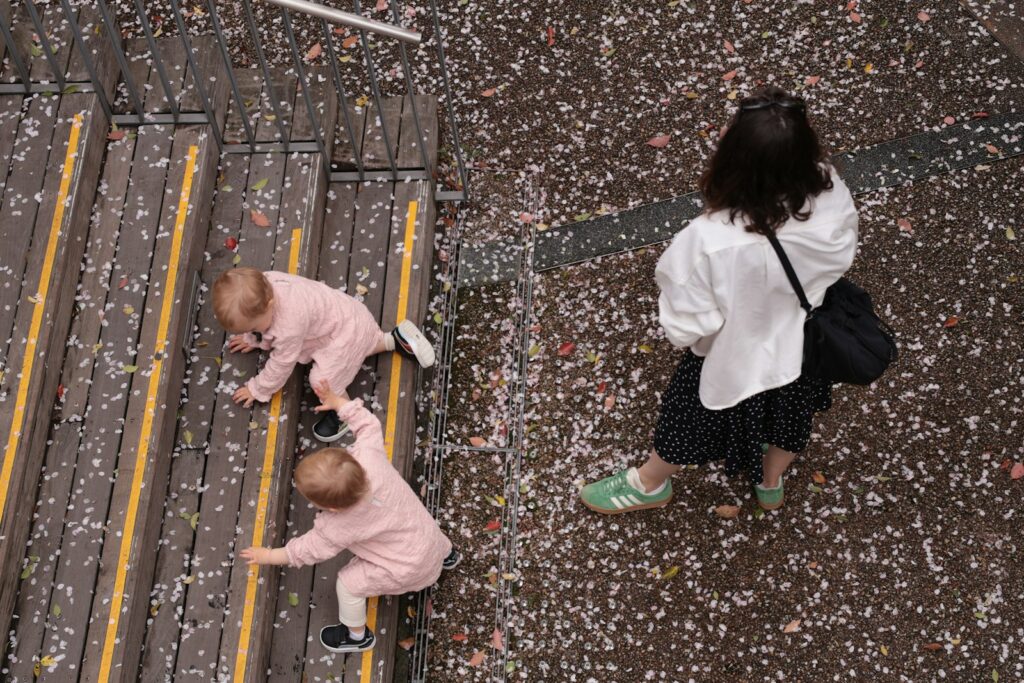 Two babies climbing stairs while a woman watches closely